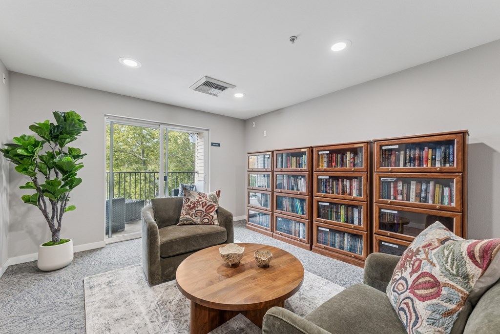 A living room with a grey couch, a wooden coffee table, a green plant, and a bookshelf filled with books.