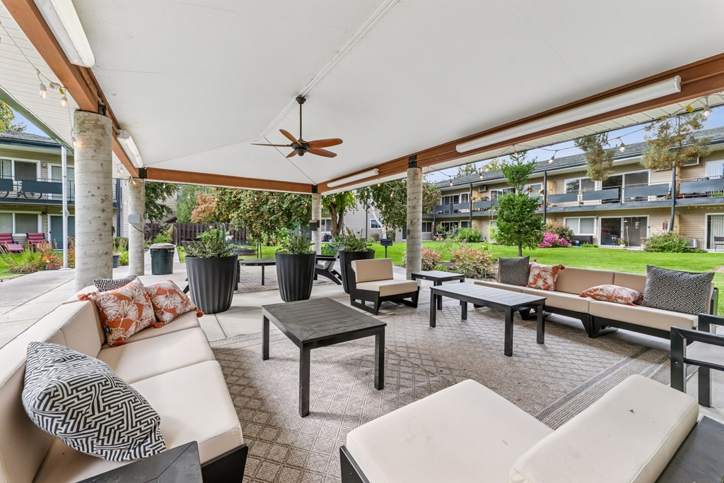 A patio with a white couch, black and white pillows, and a ceiling fan.