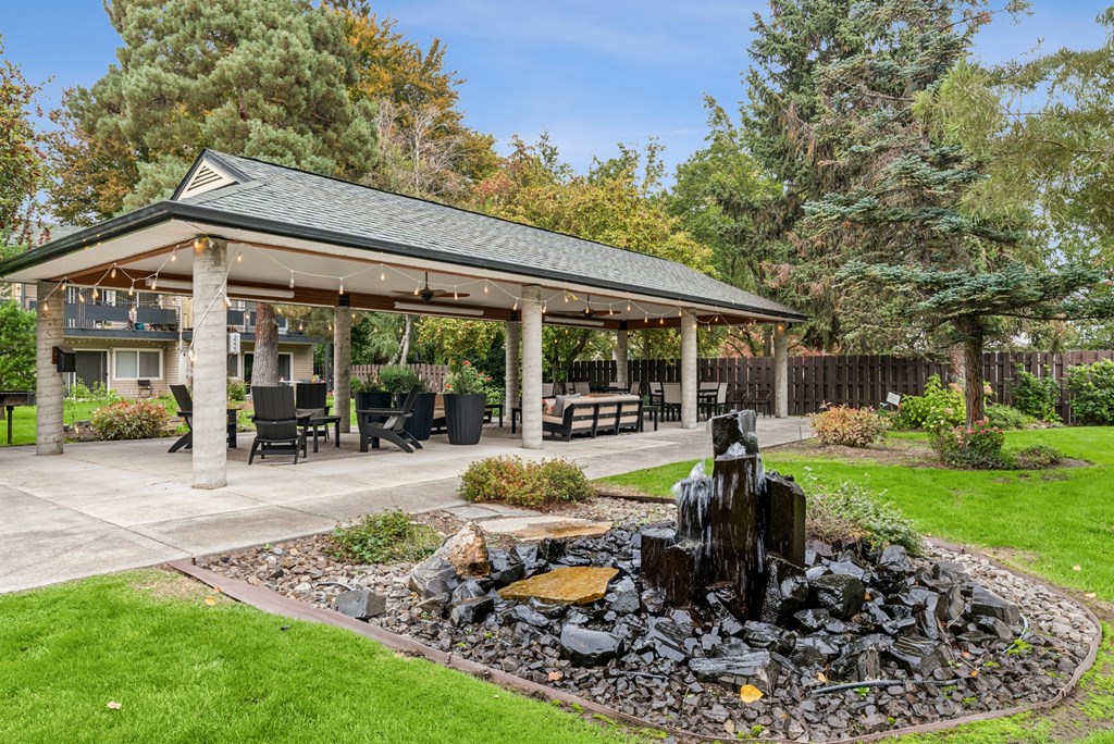 A gazebo is surrounded by a rock fountain and a grassy area.