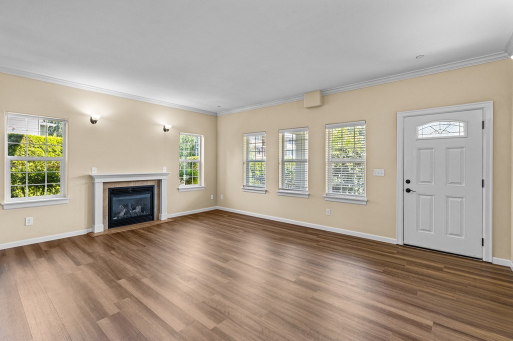 Little Tuscany Apartments & Townhomes - Living Room showing fireplace, multiple windows and front door. Vinyl plank wood flooring, white woodwork