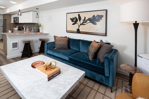 A living room with a blue couch and a painting on the wall.