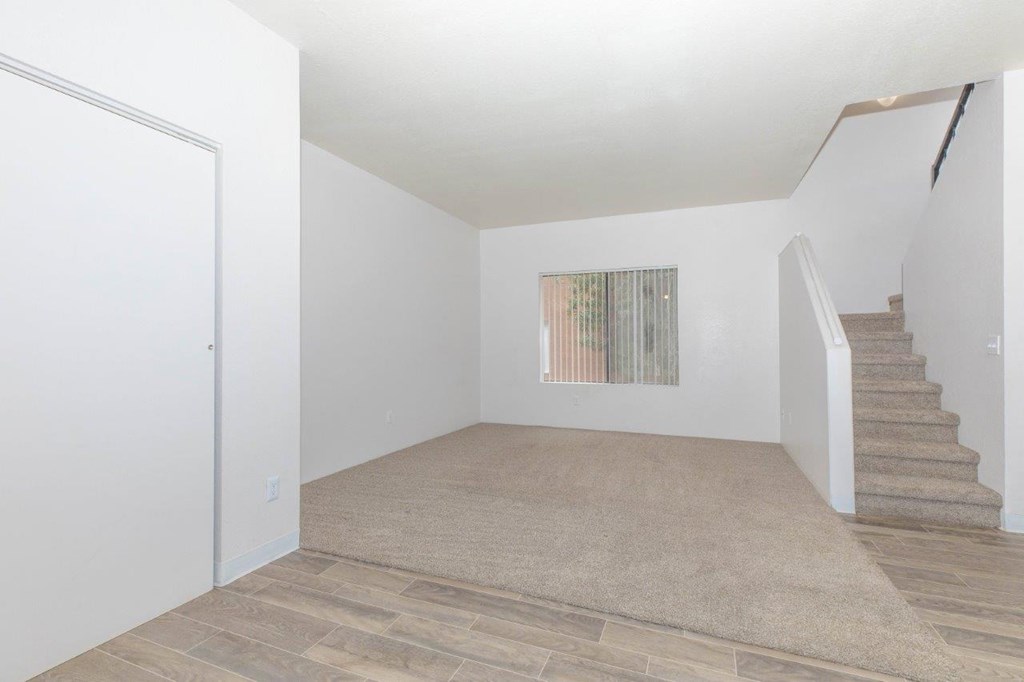 A room with a staircase and a window with vertical blinds.