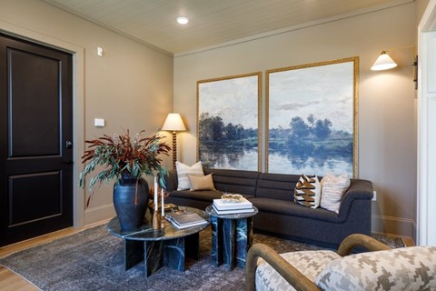 A living room with a grey couch, a black door, and a painting on the wall.