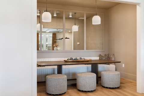A dining area with a long table and grey ottoman.