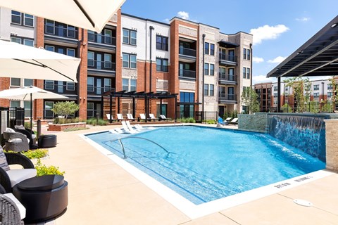 A pool surrounded by a patio with chairs and umbrellas.