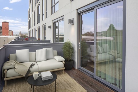 A white couch with a grey throw is on a balcony with a table in front of it.