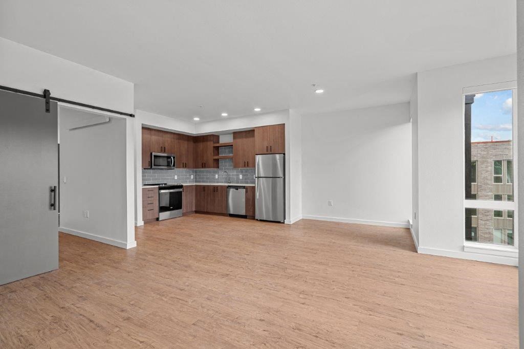 an empty living room with a kitchen with a stainless steel refrigerator