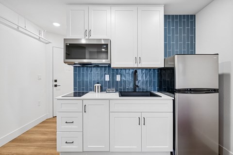 A kitchen with white cabinets and a blue tile backsplash.