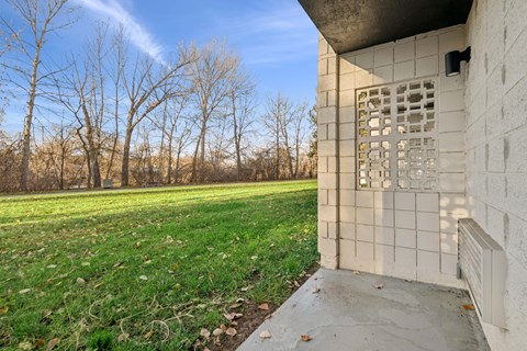 A concrete building with a window and a door is in the foreground with a grassy field and trees in the background.