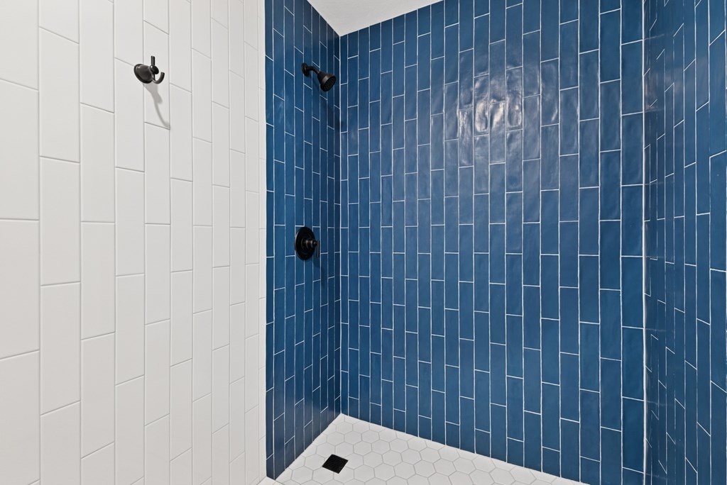 A blue tiled shower with a white tile floor.