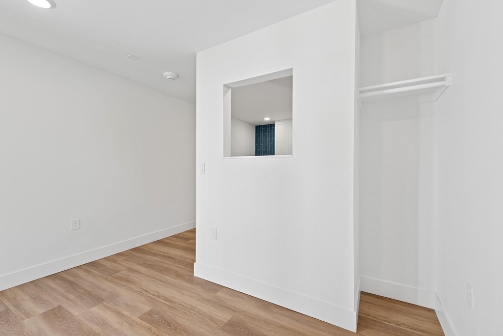 A white room with a small window and wooden flooring.