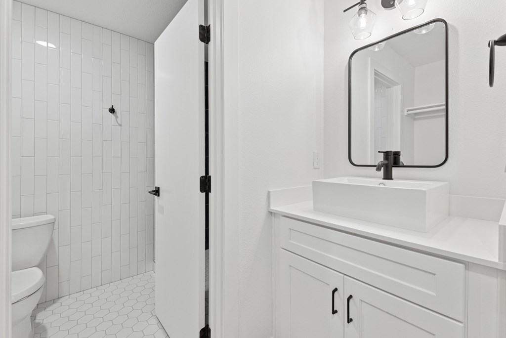 A white bathroom with a sink, mirror, and toilet.