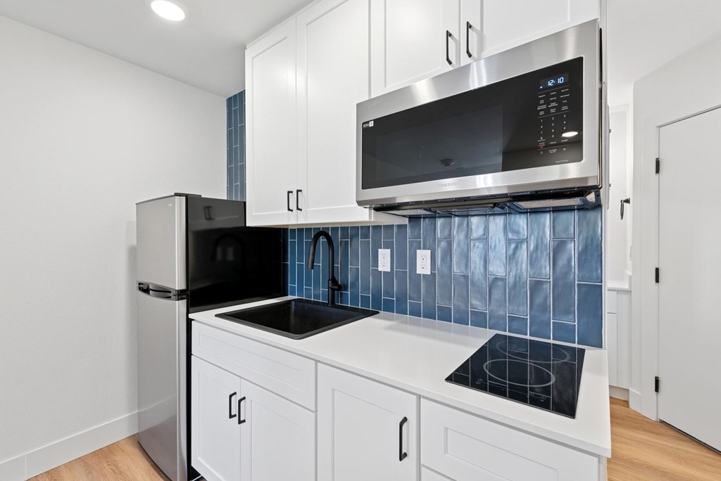 A kitchen with white cabinets and a black fridge.