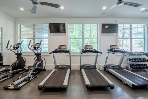 A gym with treadmills, elliptical machines, and a fan.