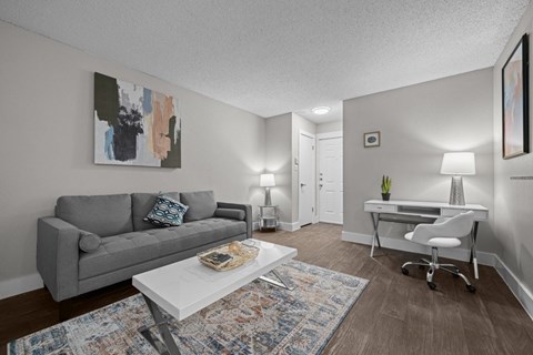 A living room with a grey couch, a white desk, and a painting on the wall.