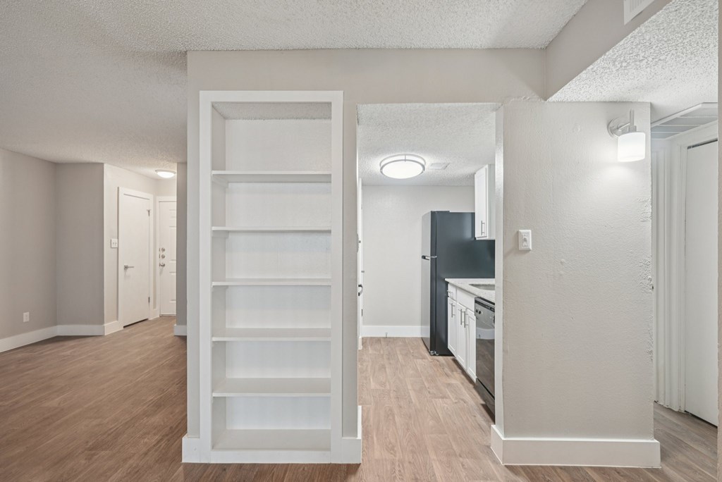 A white shelving unit in a room with a kitchen in the background.