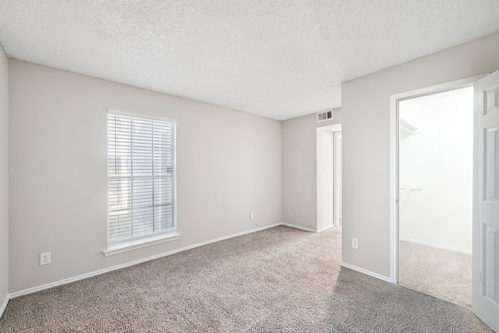 A room with a carpeted floor and a window with blinds.
