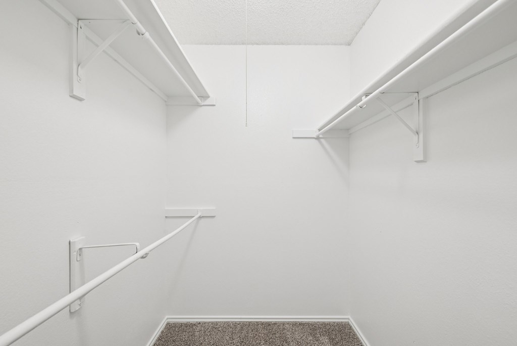 A white closet with a carpeted floor and white shelves.