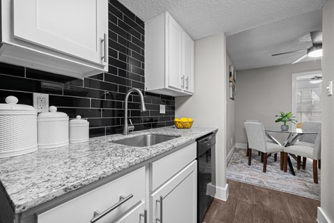 A kitchen with white cabinets and a black tile backsplash.