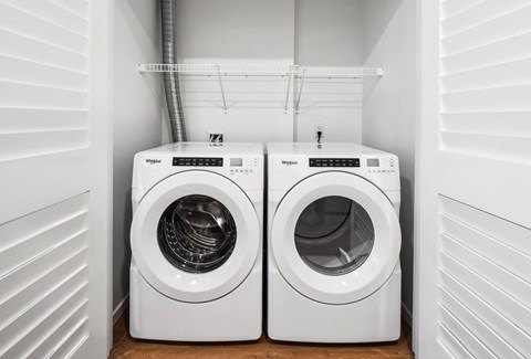 Two white Whirlpool washing machines in a small laundry room.
