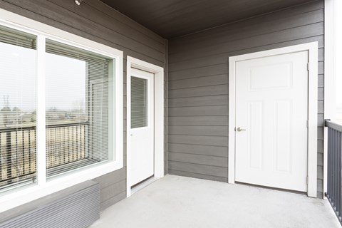 A balcony with a white door and a window with a view of a fence and trees.