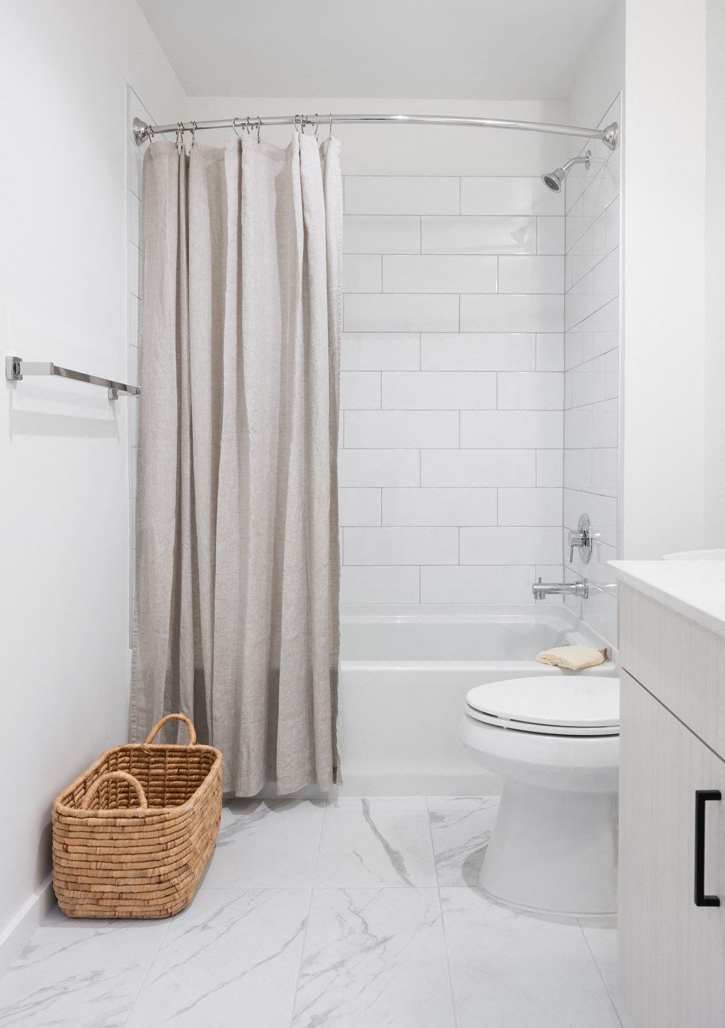 A white bathroom with a toilet, a shower curtain, and a basket.
