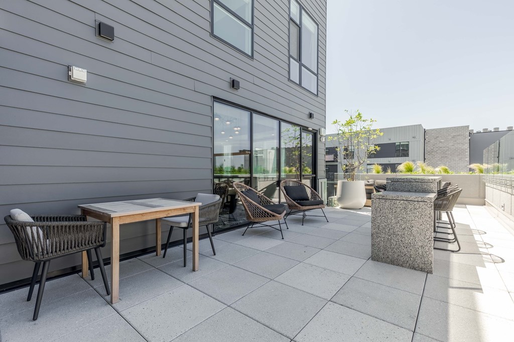 A patio with a table and chairs is in front of a grey building.