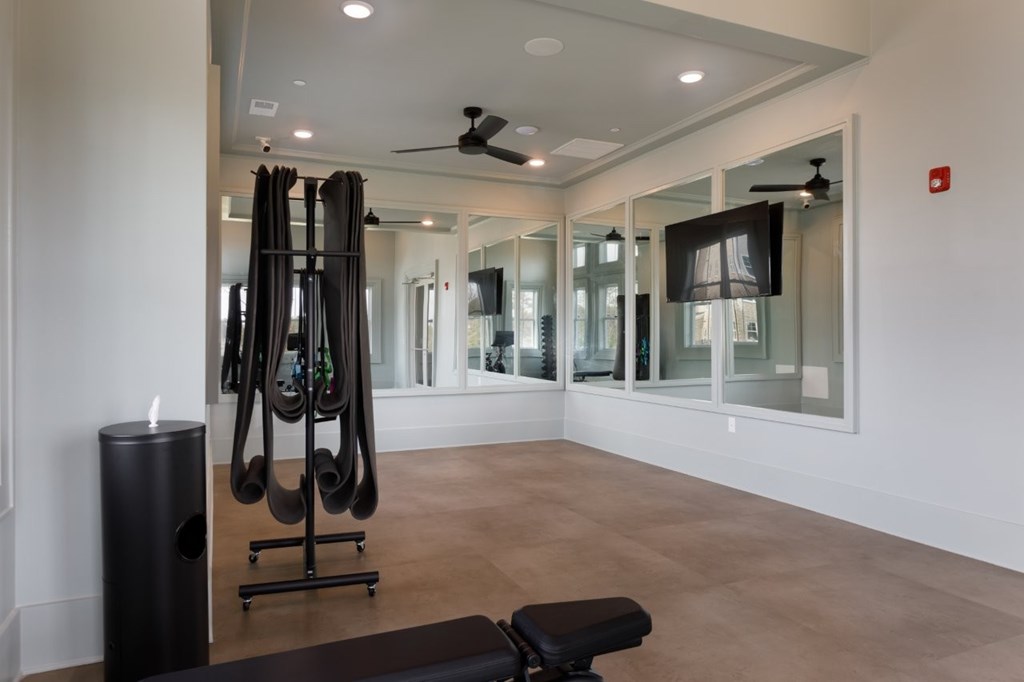 A room with a mirror, a fan, and a pair of black exercise equipment.