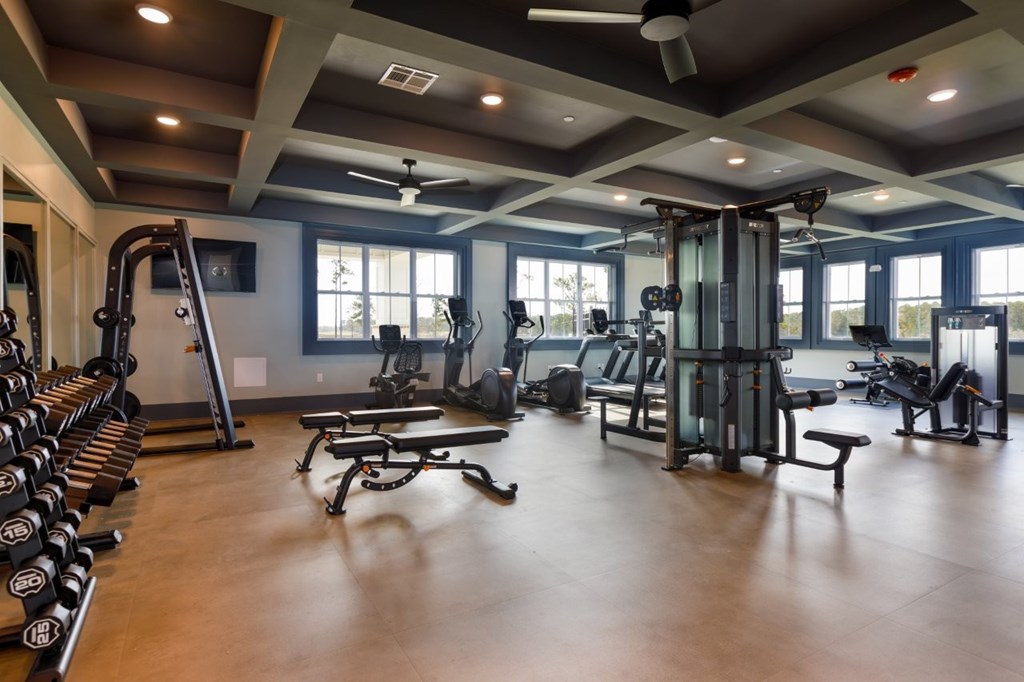 A spacious gym with a variety of equipment including dumbbells, weight machines, and a bench press.