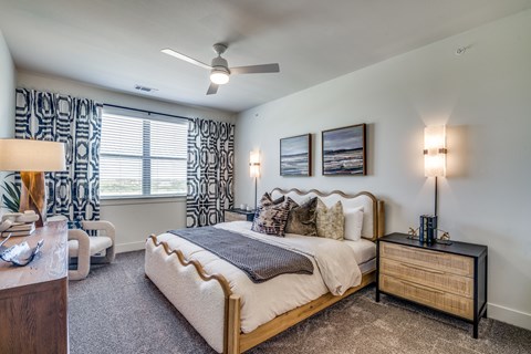 A bedroom with a large bed, a nightstand with a lamp, and a ceiling fan.
