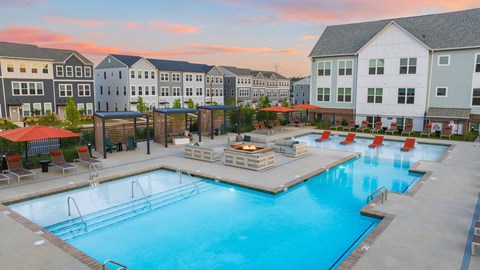 A large swimming pool surrounded by a deck with chairs and umbrellas.