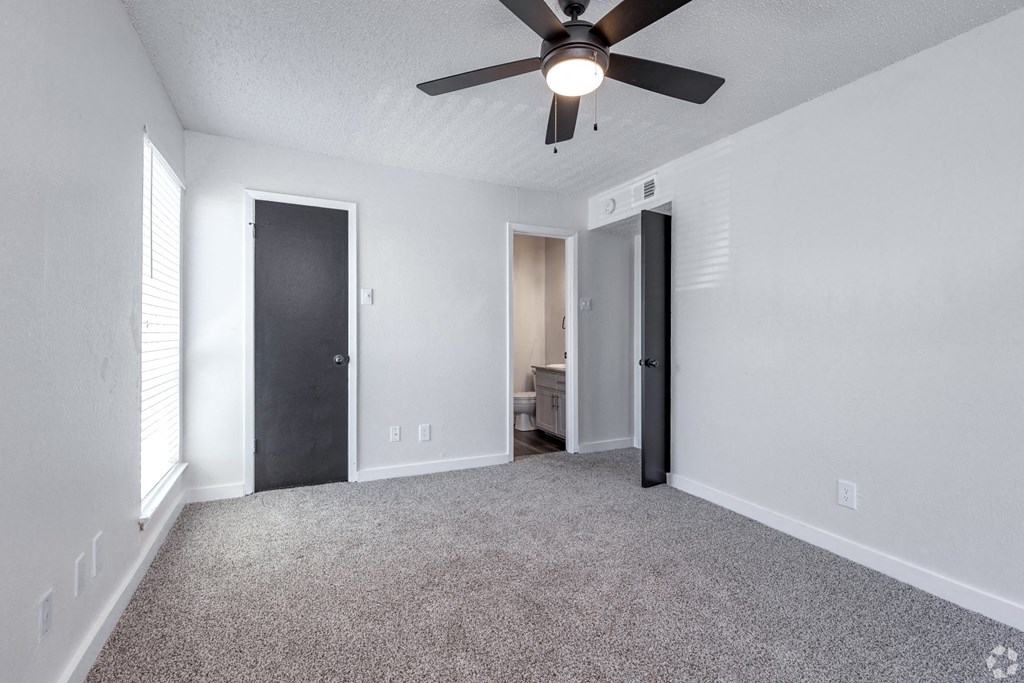 an empty living room with a ceiling fan and a door to a bathroom