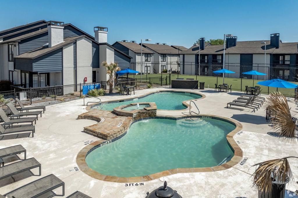 a resort style pool with chairs and umbrellas with buildings in the background