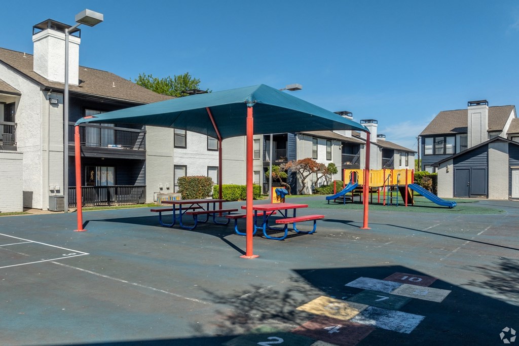 an outdoor playground with a picnic table and swing set in front of apartments