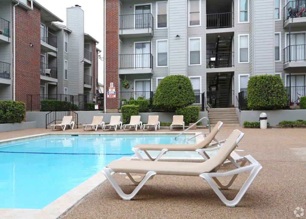 a pool with lounge chairs in front of an apartment building