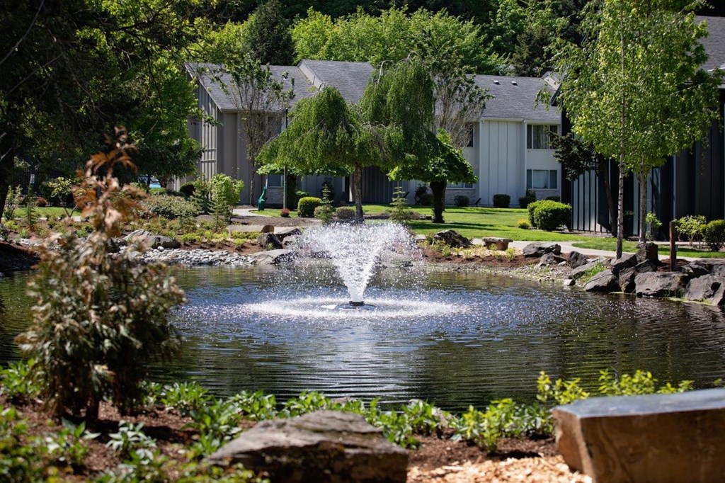 a fountain in the middle of a pond with houses in the background