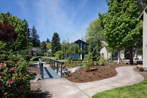 a bridge over a garden with trees and buildings in the background