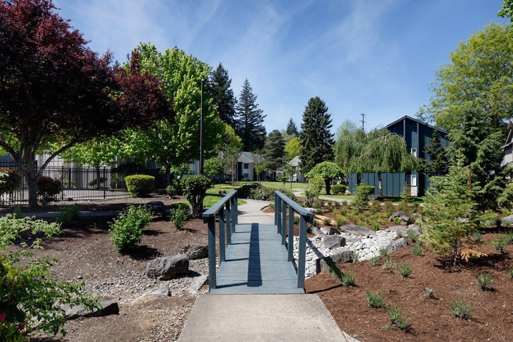 a small bridge in a park with trees and buildings in the background