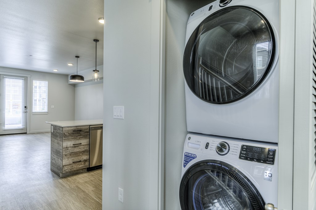 A white washing machine is in a laundry room with a wooden cabinet and a window.