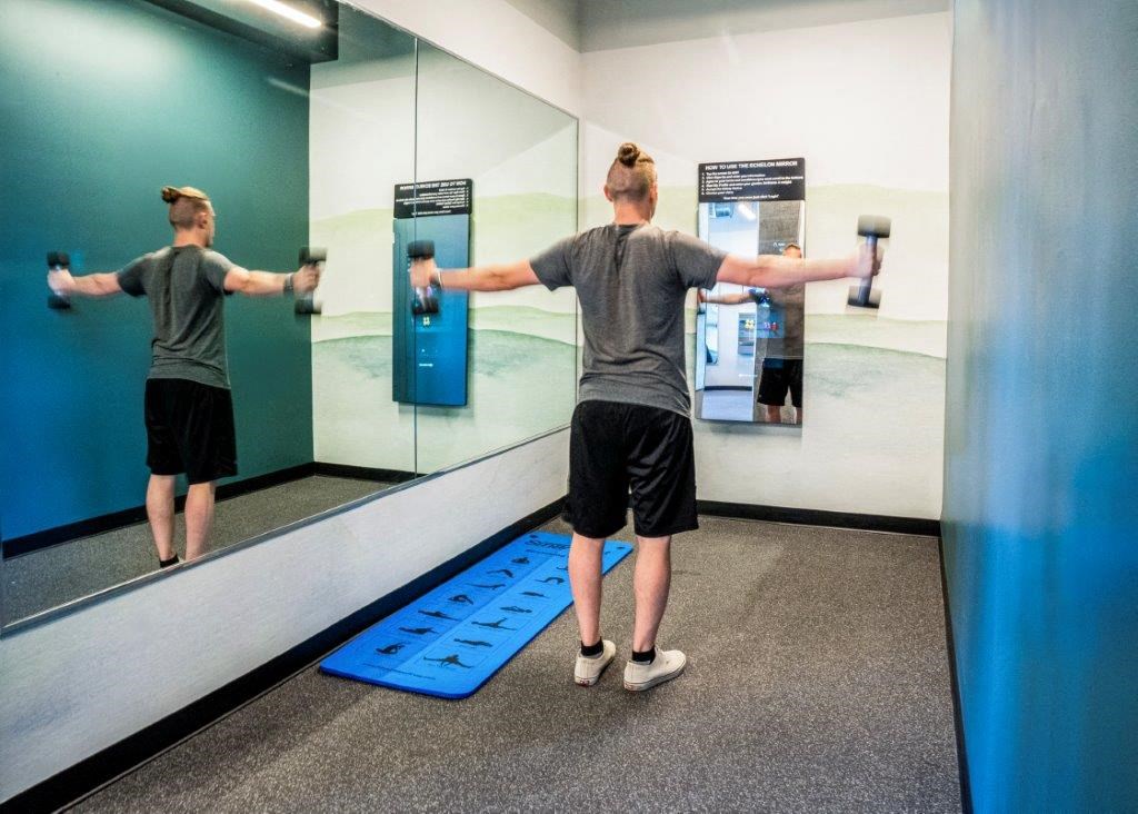 a man doing a dumbbell exercise in a mirror in a gym