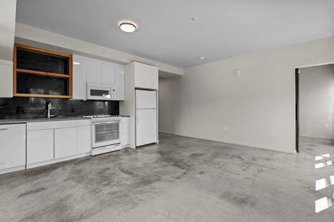 A kitchen with white cabinets and appliances, a window, and a concrete floor.