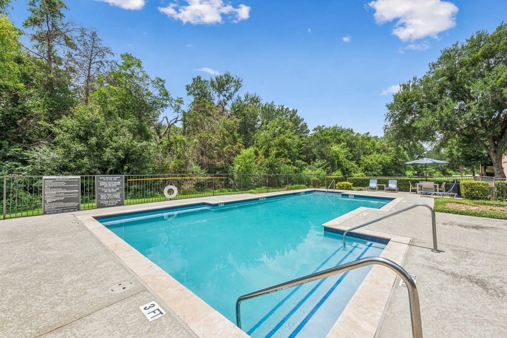 A swimming pool surrounded by trees and a clear blue sky.