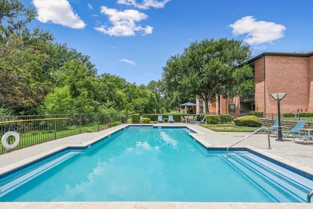 A swimming pool surrounded by trees and a building in the background.