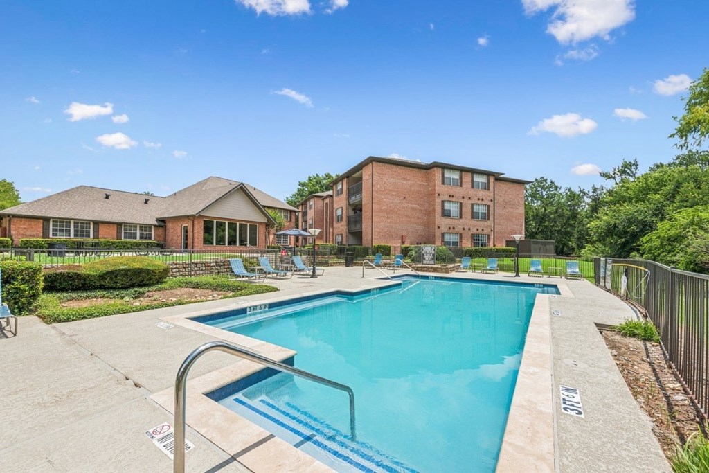 A swimming pool surrounded by a concrete patio and a brick building.