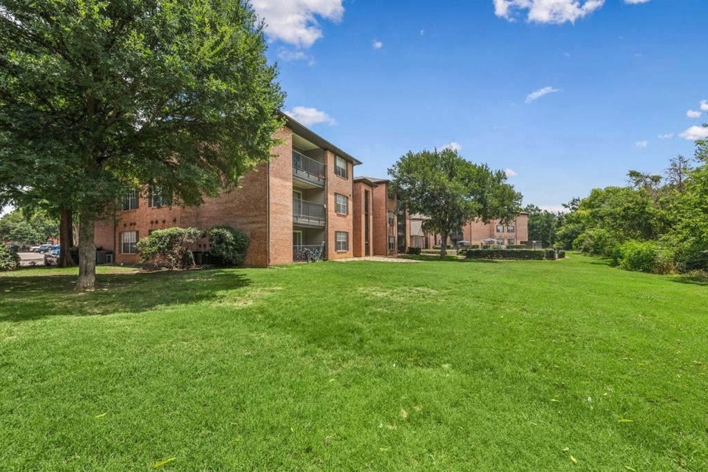 A grassy area in front of a brick building with trees.