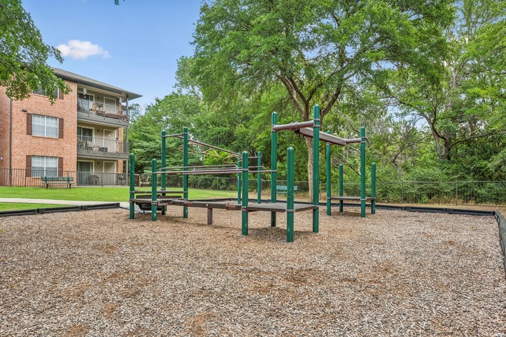 A playground with a green swing set and a brown gravel ground.