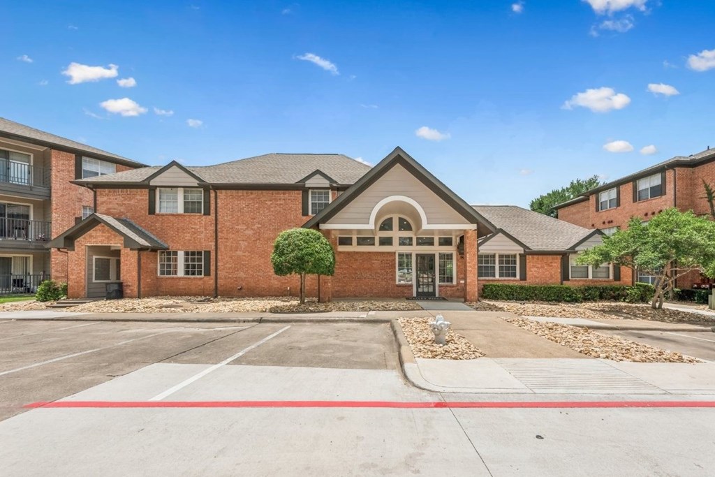 A building with a red brick facade and a large front yard with a tree and a fire hydrant.