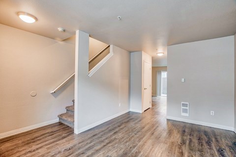 A spacious room with wooden floors and a staircase leading to another room.