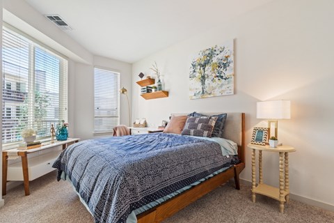 A bedroom with a bed, nightstand, and a painting on the wall.