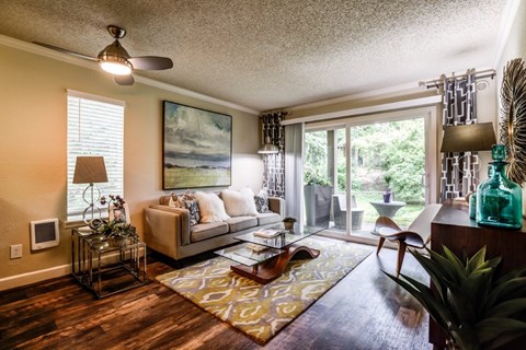 A living room with a couch, a rug, a fan, and a painting on the wall.